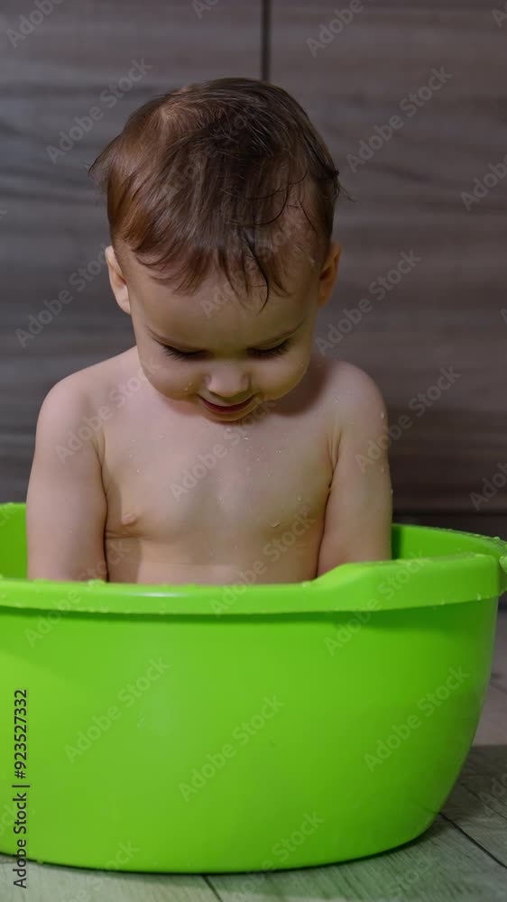 Smiling Caucasian baby sits in the green washbowl. Kid looks down at the water and then up with interest. Smiling Caucasian baby sits in the green washbowl. Kid looks down at the water and then up with interest.