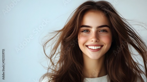 Beautiful young woman with long flowing hair, radiant smile, white background, copy space for text, hair in motion, soft natural lighting, glowing skin, white casual top, carefree expression.