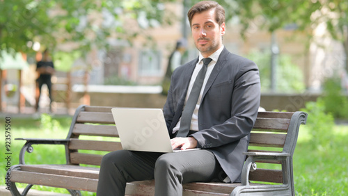 Middle Aged Businessman Looking at Camera while Using Laptop Outdoor