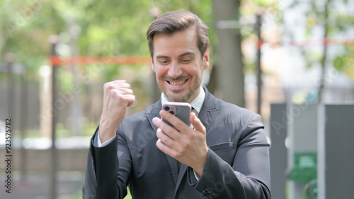 Portrait of Young Businessman Excited for Results on Phone Outdoor