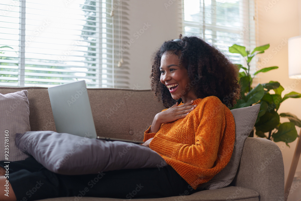 Smiling African American woman enjoying online content on laptop while relaxing on comfortable couch at home. Smiling African American woman enjoying online content on laptop while relaxing on comfortable couch at home.