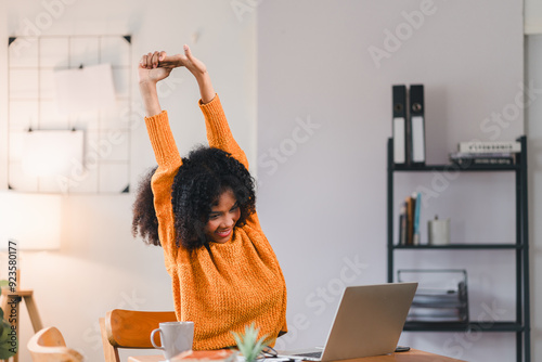 African American woman stretching her arms while taking break from working on laptop at home. photo