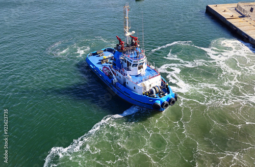A tugboat in port stands ready alongside the ship waiting to provide support

