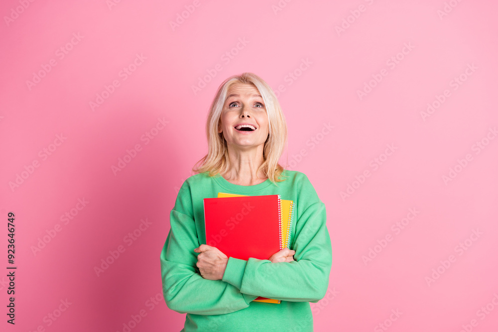 Photo of attractive retired woman hold copybook look up empty space dressed stylish green clothes isolated on pink color background Photo of attractive retired woman hold copybook look up empty space dressed stylish green clothes isolated on pink color background