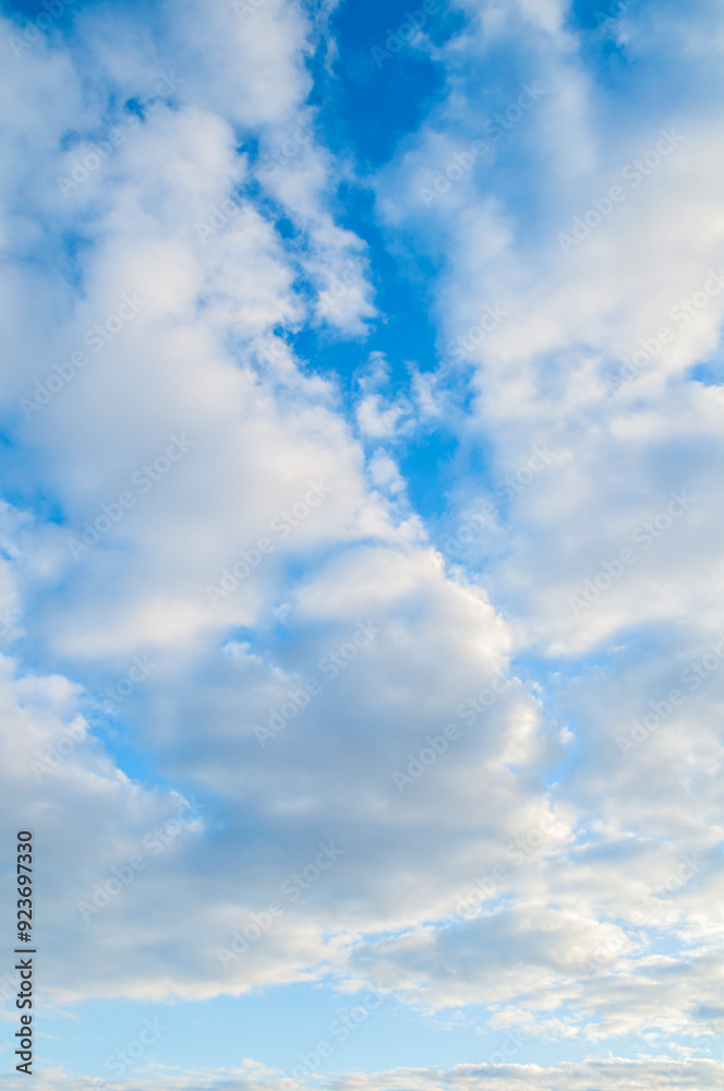 Fototapeta premium Blue cloudy sky background. Blue sky landscape with picturesque sunset clouds lit by evening sunset light - evening blue cloudy sky view