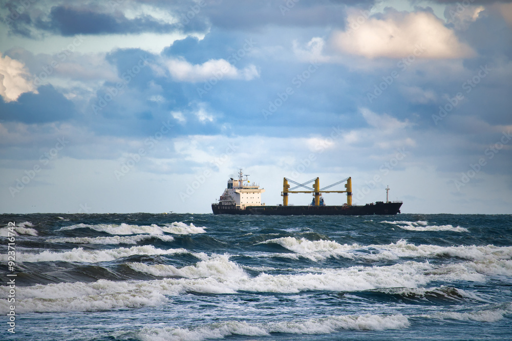 Cargo ship navigating through rough ocean waves under a dramatic cloudy sky at sea Cargo ship navigating through rough ocean waves under a dramatic cloudy sky at sea