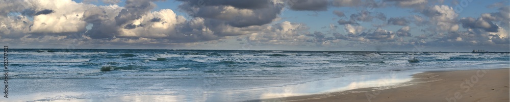 Panoramic view of a dramatic ocean scene with crashing waves under a cloudy sky