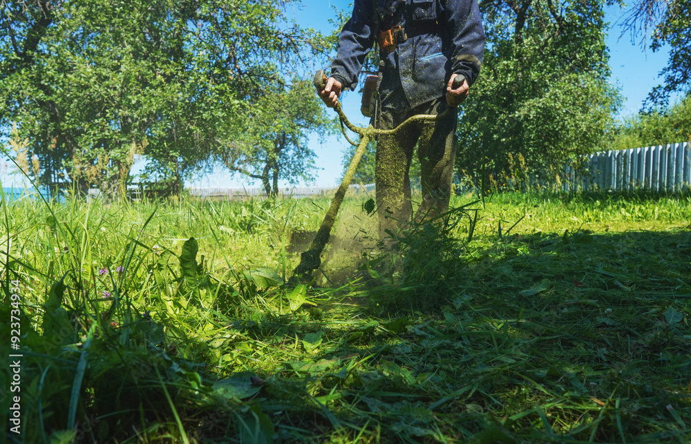 Grass Trimmer and Grass Cutter. Gardener mows weeds grass. Man cutting grass in yard by using string trimmer. Worker lawn mower cutting green garden. Lawn mowing machine. lawn maintenance service. Grass Trimmer and Grass Cutter. Gardener mows weeds grass. Man cutting grass in yard by using string trimmer. Worker lawn mower cutting green garden. Lawn mowing machine. lawn maintenance service.