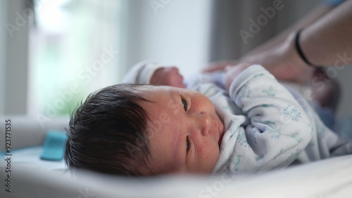 Close-up of newborn baby on a changing table, looking up, with mother holding baby's legs, capturing the interaction and bond during a routine diaper change in a home setting