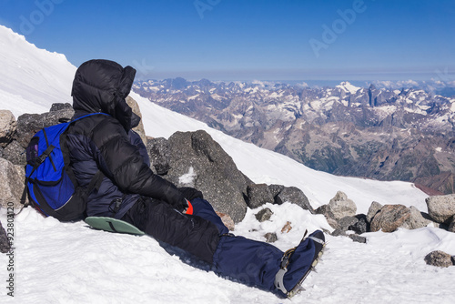 mountaineer rests sitting on a snowy slope among rocks in the highlands