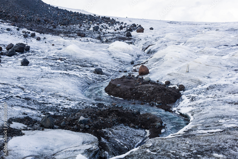 streams of water on the surface of a melting highland glacierб rocks and soil under ice become visible