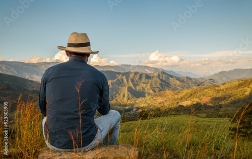 Man enjoying serene mountain landscape at sunset. Peaceful outdoor scene with person in hat looking at scenic view. Tranquility and nature appreciation