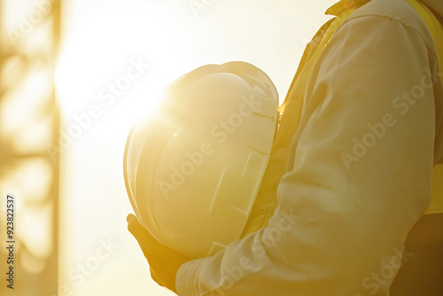 A technician holds a white safety hard hat against a backdrop of bright sunlight. photo