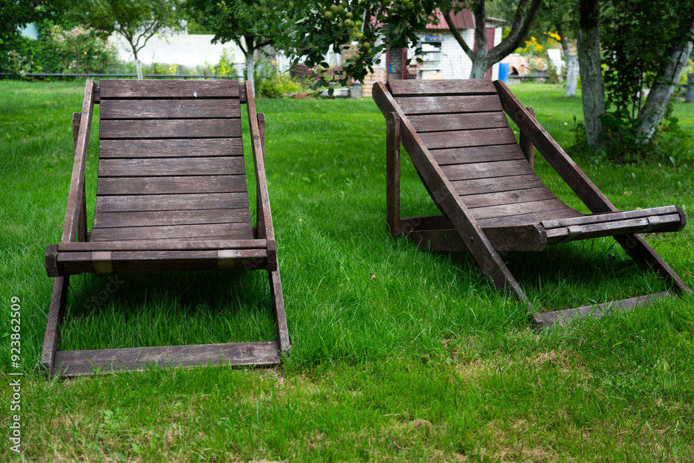 Two wooden deck chairs stand in the garden on the grass Two wooden deck chairs stand in the garden on the grass