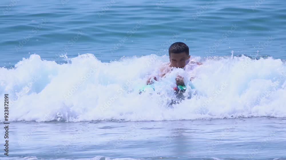 Young handsome man is swimming on the board in the waves of the sea surf and enjoys a vacation. High quality 4k footage