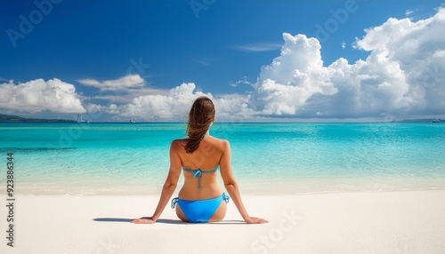 brunette woman wearing blue bikini relaxing on the white sand on the tropical beach