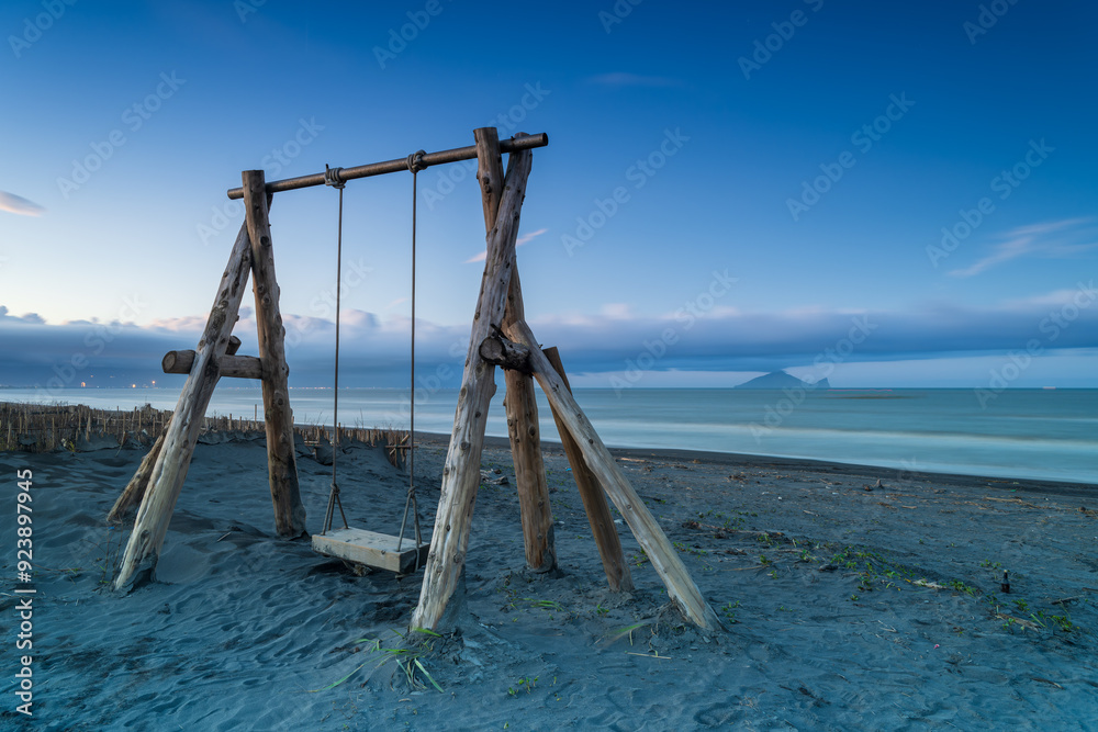 A solitary wooden swing set beckons on a tranquil beach. In the distance, the Turtle Island is partially veiled by clouds, creating a serene coastal landscape. Zhuangwei, Yilan County, Taiwan. A solitary wooden swing set beckons on a tranquil beach. In the distance, the Turtle Island is partially veiled by clouds, creating a serene coastal landscape. Zhuangwei, Yilan County, Taiwan.