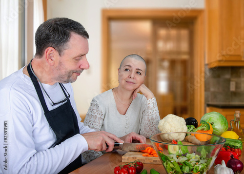 Cooking with Compassion: Husband Prepares Meal in Kitchen, Wife Undergoing Cancer Treatment Admires His Loving Support and Dedication.