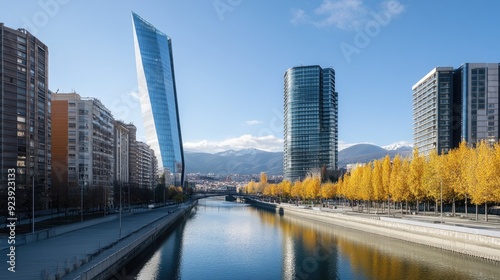 A serene river reflects modern architecture and vibrant autumn leaves under a clear sky, creating a harmonious blend of nature and urban life