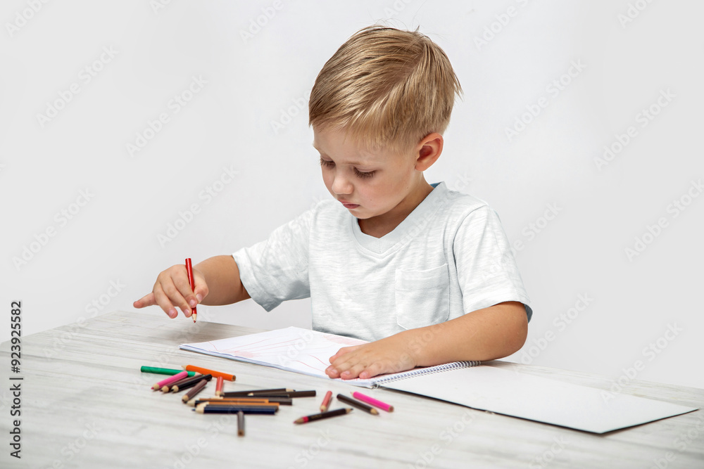 A toddler draws with colored pencils in a sketchbook while sitting at a table in the nursery. A toddler draws with colored pencils in a sketchbook while sitting at a table in the nursery.