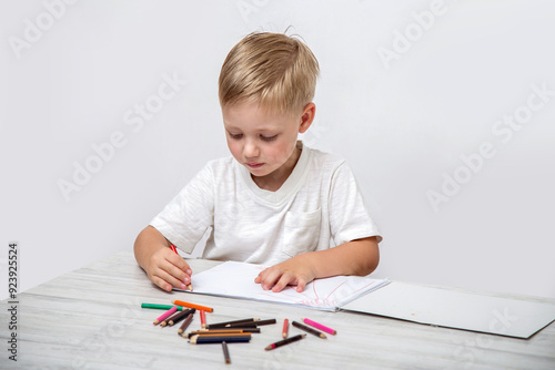 A toddler draws with colored pencils in a sketchbook while sitting at a table in the nursery.