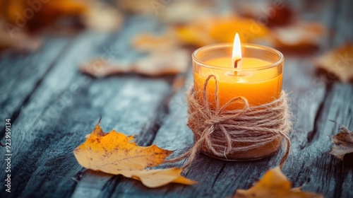 Candle wrapped in twine on a wooden table with autumn leaves, creating a romantic background