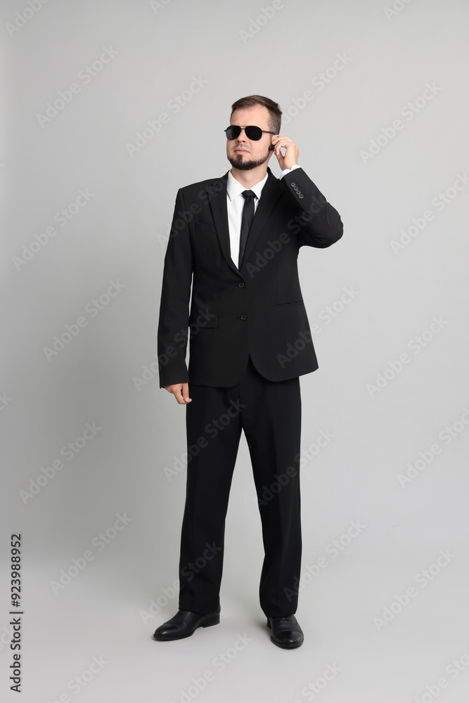 Young bodyguard in suit and sunglasses using earpiece on grey background Young bodyguard in suit and sunglasses using earpiece on grey background
