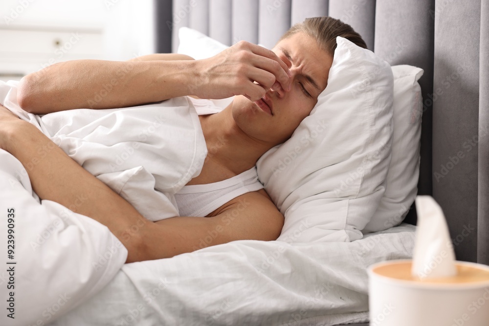 Young man suffering from sinusitis and lying in bed at home Young man suffering from sinusitis and lying in bed at home