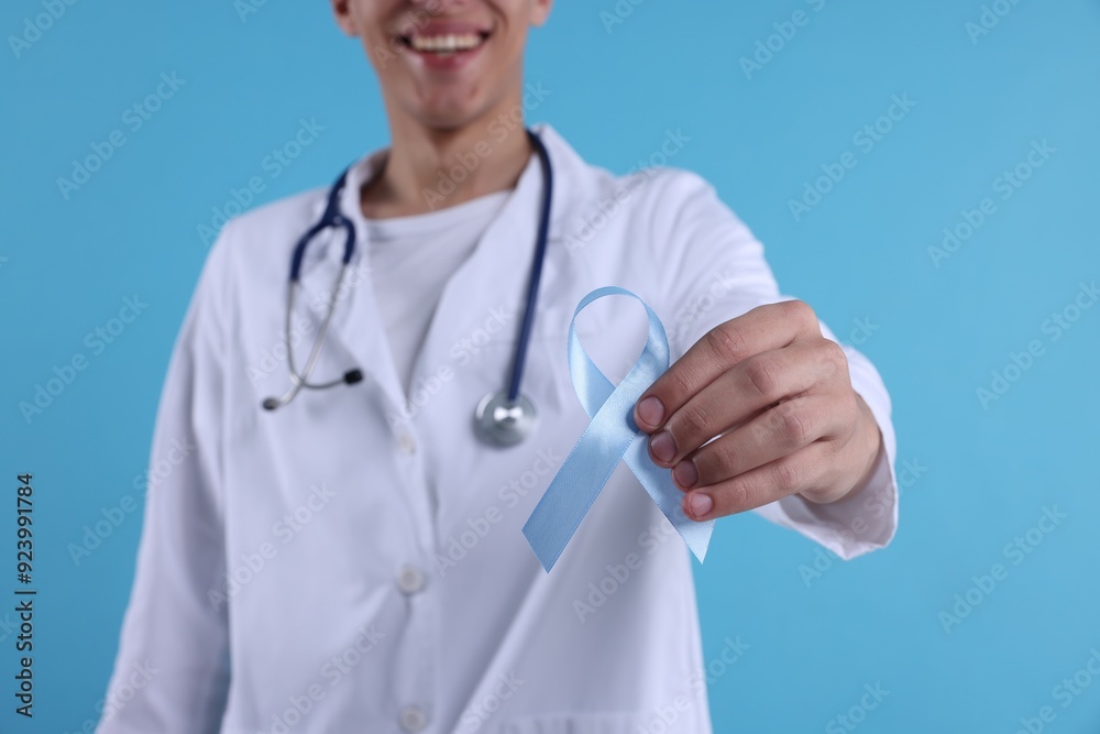Prostate cancer awareness. Doctor holding light blue ribbon as symbol of support on color background, selective focus Prostate cancer awareness. Doctor holding light blue ribbon as symbol of support on color background, selective focus