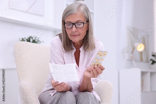 Senior woman with pills reading medicine instruction in armchair at home