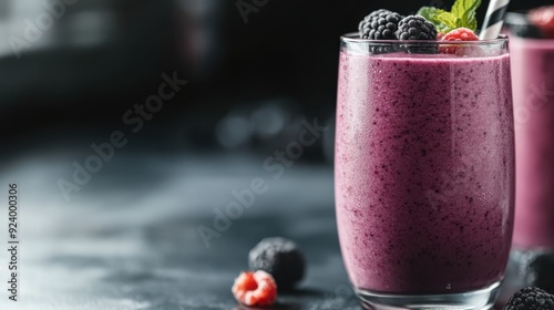 A tasty and vibrant fresh berry smoothie is served in a tall glass, garnished with mint and berries on top, presented on a dark, elegant surface with scattered berries. photo