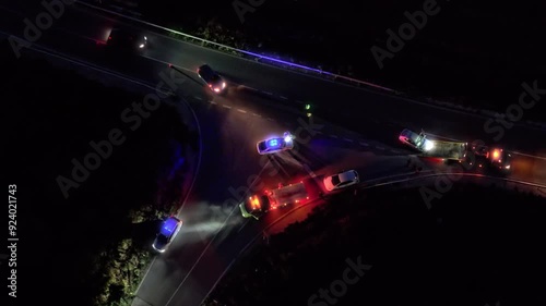 Aerial view of night car accident with involved pedestrian. Roadside assistance loads wrecked car, police direct traffic