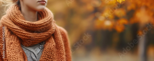 Close-up of woman's neck wrapped in orange knit scarf, autumn fashion detail with blurred fall background. Banner with copy space photo