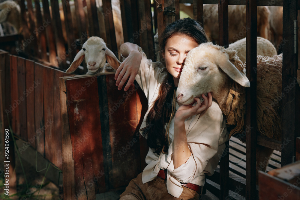 A young woman is petting a sheep in a fenced in pen with other sheep in the background