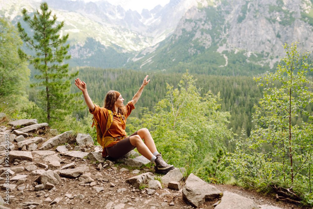 Naklejka premium Smiling female with backpack on hike in nature. Beautiful woman hiker standing on mountain trail and looking at camera smiling. Lifestyle, adventure, nature, active life.