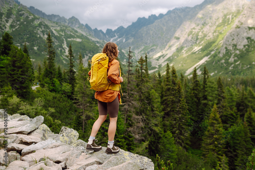 Smiling female with backpack on hike in nature. Beautiful woman hiker standing on mountain trail and looking at camera smiling. Lifestyle, adventure, nature, active life. Smiling female with backpack on hike in nature. Beautiful woman hiker standing on mountain trail and looking at camera smiling. Lifestyle, adventure, nature, active life.