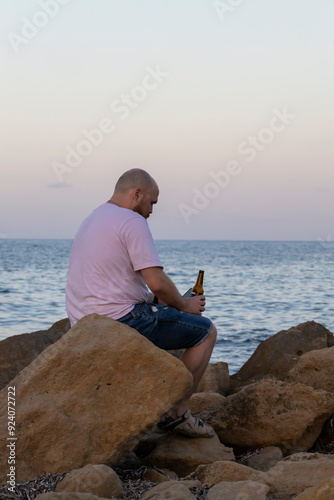 Man with cell phone on the beach drinking a bottle of beer.