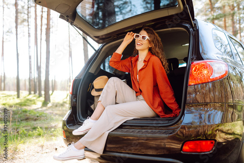 Happy woman enjoying nature while sitting in the trunk of her car during a solo trip. Road trips summer holidays.