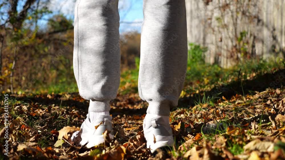 Close up to male feet in sneakers going along trail on fallen dry leaves. Legs of young man stepping along path outdoor. Guy walking at nature sunny autumn day. Low view Slow motion Close up to male feet in sneakers going along trail on fallen dry leaves. Legs of young man stepping along path outdoor. Guy walking at nature sunny autumn day. Low view Slow motion
