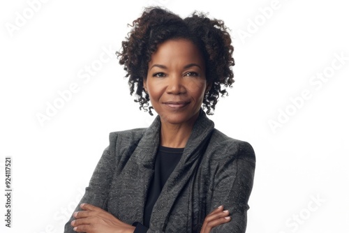 A woman with short, curly black hair is wearing a grey blazer and looking directly at the camera with a confident smile