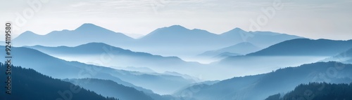 Serene mountain landscape with layers of mist and blue hues, conveying tranquility and natural beauty in a panoramic view of undulating peaks.