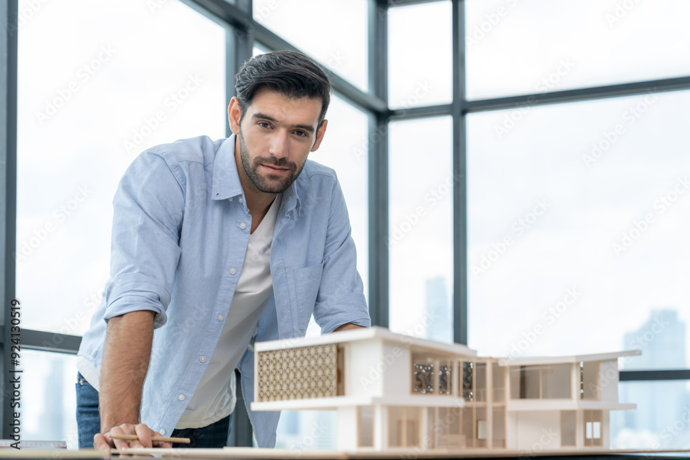 Smiling caucasian architect engineer looking at camera while standing with house model. Smart interior designer standing while holding pencil. Project plan, civil engineering, worker. Tracery. Smiling caucasian architect engineer looking at camera while standing with house model. Smart interior designer standing while holding pencil. Project plan, civil engineering, worker. Tracery.
