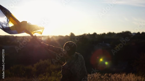 Ukrainian army man waving national banner against background of sunset. Young male soldier lifted flag at countryside. Victory against russian aggression. End of war between russia and Ukraine photo