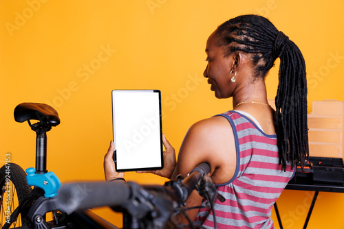 Detailed shot of black woman carrying a device displaying blank copyspace mockup template and damaged bicycle nearby. For bike maintenance, female cyclist holds a tablet with a chromakey whitescreen. photo