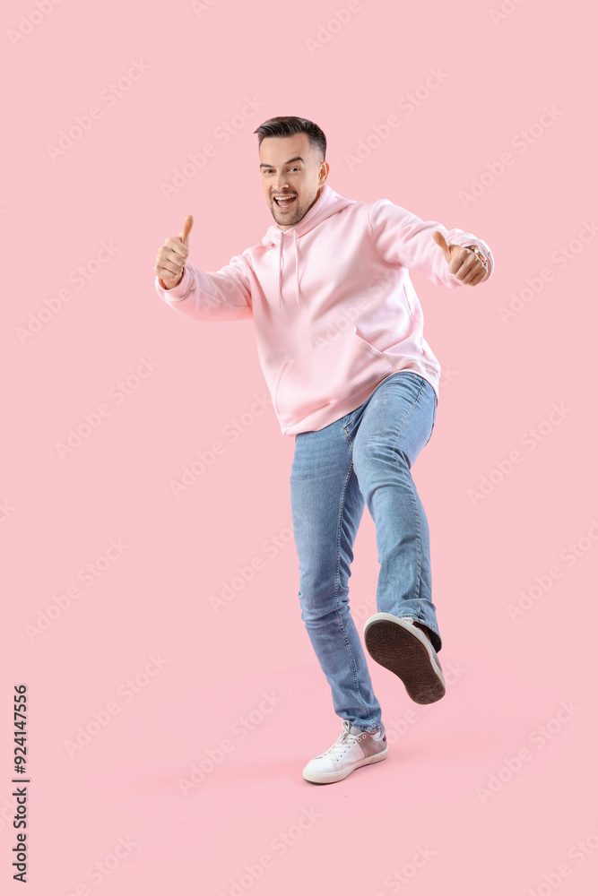 Happy young man showing thumbs-up on pink background