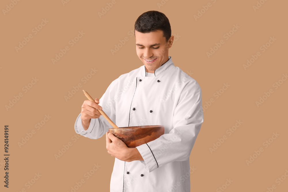 Handsome happy male chef with bowl and spoon on brown background Handsome happy male chef with bowl and spoon on brown background