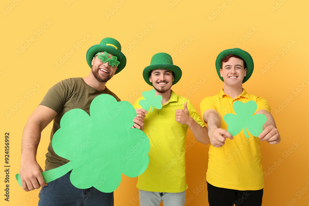 Happy young men in leprechaun's hats with clovers on yellow background. St. Patrick's Day celebration