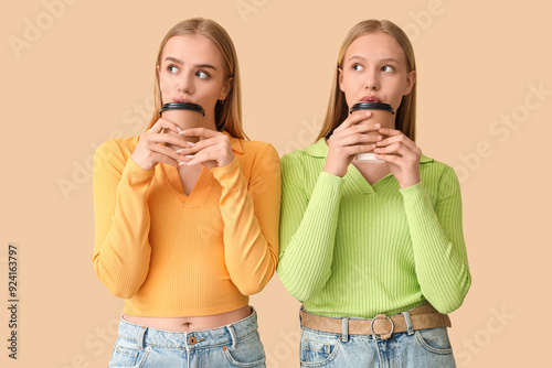 Beautiful young sisters with cups of coffee on beige background