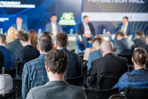 Business professionals attending a seminar, listening to a panel discussion. Focus on audience and speaker engagement.