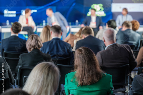 Audience members are attentively listening to a panel discussion at a business conference, focusing on various topics presented by speakers on stage.